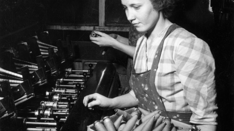 Henkilö istuu kudontalaitteen äärellä. Vanha valokuva.