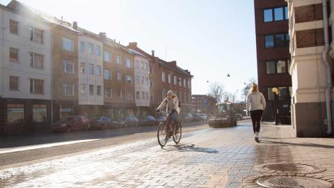 Pyöräilija, jalankulkija ja harjaustraktori kadulla.
