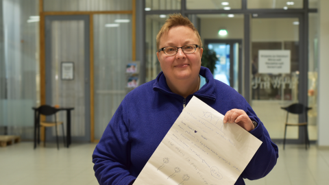 Henkilö seisoo aulassa. Hänellä on kädessään juliste.