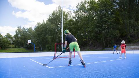 Kolme eri-ikäistä pelaajaa pelaa mailojen kanssa sinipohjaisella kentällä ulkona.
