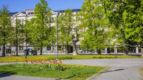Kuvassa vihreää puistoa, käytäviä, tulppaaneja ja taideteos.