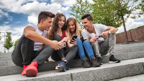 Neljä nuorta istuvat kivisillä portailla. Kaksi selaa kännykkää ja muut katsovat.