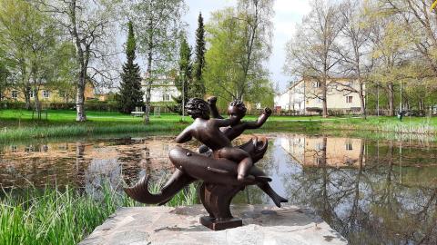 Kahta kaloilla ratsastavaa poikaa esittävä veistos lammen rannalla.