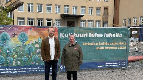 Jaani Haapasalo ja Annamaija Saarela seisovat ulkovaatteissa Nekalan kulttuurikeskuksen työmaan edessä. Taustalla lakana, jossa lukee "Kulttuuri tulee lähelle".