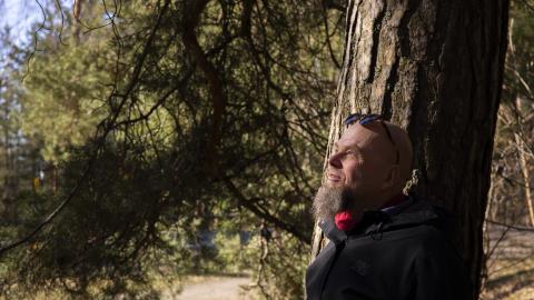 Henkilö nojaa vanhan puun runkoon, jonka oksat täyttävät kuvan taka-alan.