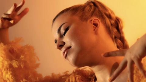 A young woman dances against an orange background.