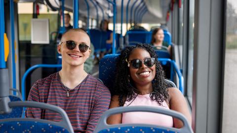 Tyttö ja poika bussissa, aurinkolasit silmillä.