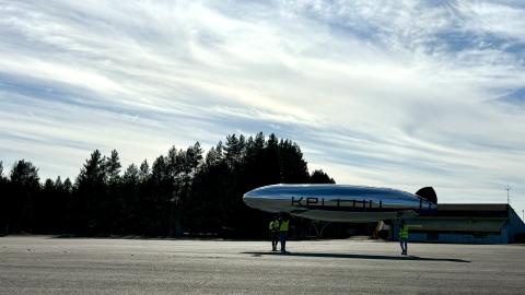 Ilmalaiva maatasolla, henkilöt pitävät siitä kiinni.