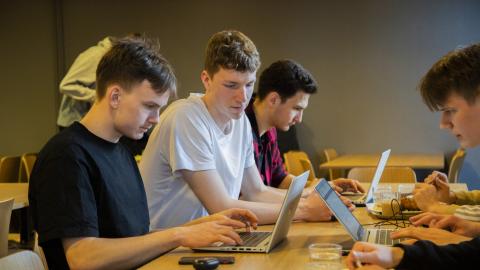 Ryhmä lukio-opiskelijoita opiskelee pöydän ympärillä.