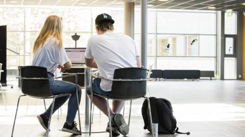 Two students are sitting at a table in the school lobby.