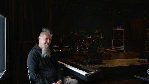 Parrakas henkilö istuu koskettimien edessä tummassa huonessa.