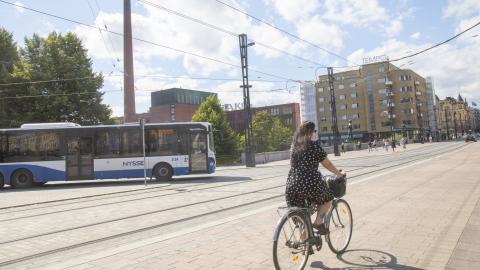Bussi kääntymässä Hämeenkadulle ja pyöräilijä etualalla, taivaalla kesäpilviä.