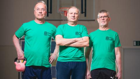 Three people are standing in a line. Two of them are holding kettlebells in their hands.