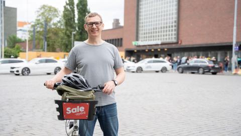 Henkilö rautatieaseman edustalla kaupunkipyörän kanssa.