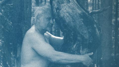 A blue-tinted photograph of an old man hugging a tree.