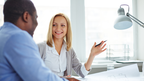 Kaksi henkilöä istuvät pöydän ääressä. He hymyilevät toisilleen ja keskustelevat.