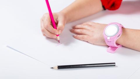 Nuori käsi kirjoittaa punaisella värikynällä paperille. Toisessa kädessä on vaaleanpunainen älykello