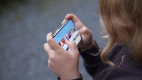 Lapsi pitää puhelinta sormet koukussa ja katsoo ruutua.