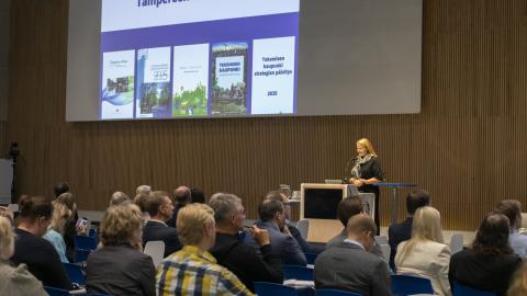 Yleisö katsomossa istumassa ja kuuntelemassa puhujaa.