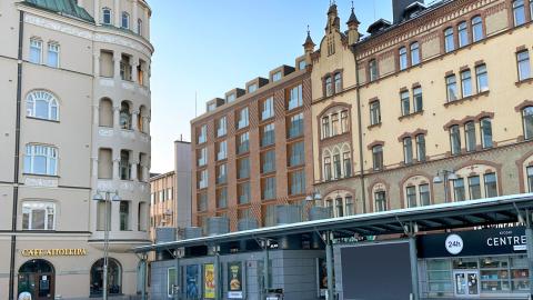 Kuvassa vanhoja kerrostaloja, keskellä uuden rakennuksen havainnekuva, etualalla torin kioski.