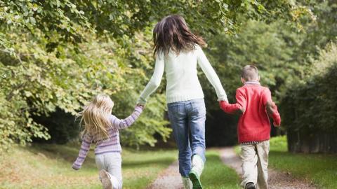 An adult and two children running hand in hand on a summer forest path.