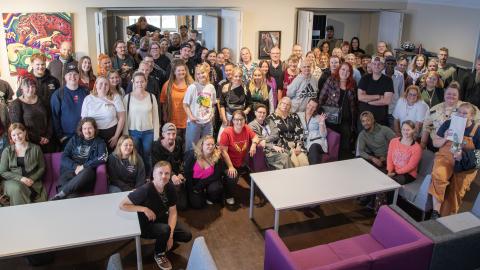 kuvassa iso joukko nuorisopalveluiden työntekijöitä. Osa istuu sohvilla ja osaa seisoo