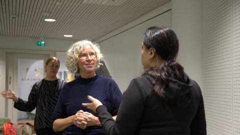 A blonde-haired woman and a dark-haired woman are talking to each other.