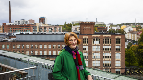 A person is standing on a rooftop terrace with the old red-brick Tampella factory building behind them, which has a large Tamperella sign on the roof.