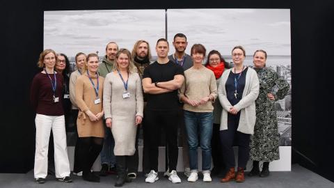 Kolmetoista henkilöä seisoo pienellä korokkeella. Taustalla ilmakuvaa Tampereen keskustasta.