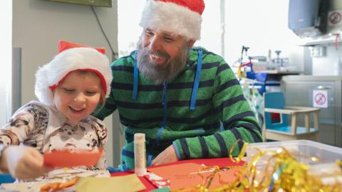 Pieni tyttö ja mies askartelevat korttia iloisina tonttulakit päässään.