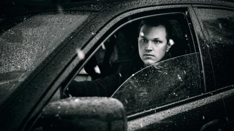 Mustavalkoisessa kuvassa Harry-Pekka on sateisen auton sisällä, etuoven lasi auki.