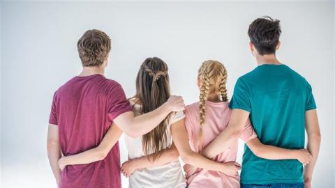 Four young people have their backs to the spectator. They are holding hands behind their backs.