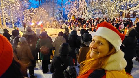 A crowd of people watching a fire show in a snowy landscape. In the foreground, a woman in an elf costume looks at the camera.