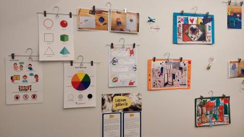 Vaalealla seinällä on mm. värikkäitä lasten tekemiä kollaaseja ja väriympyrä.