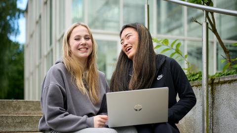 Two people are sitting on the stairs, smiling. One has a laptop on his lap.