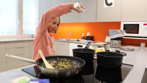 Kouluikäinen tyttö maustaa ruokaa kasvisruokakurssilla.