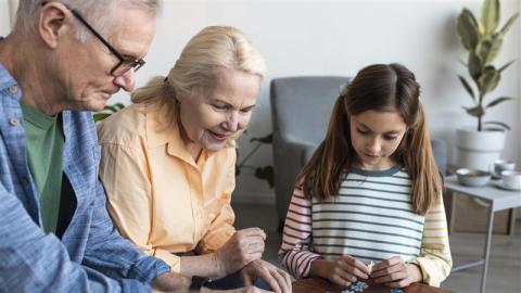 Isoäiti ja isoiso istuvat sohvapöydän ääressä kokoamassa palapeliä tummahiuksisen lapsen kanssa.