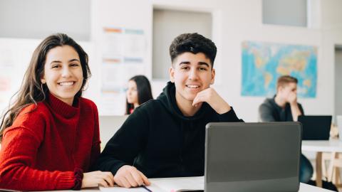 kuvassa kaksi henkilöä istuu luokkahuoneessa tietokoneen ääressä.