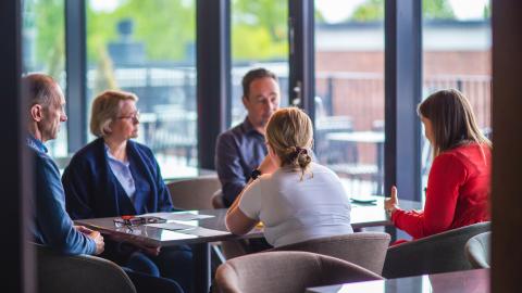 Kuvassa viisi henkilöä istuu pöydän ääressä.