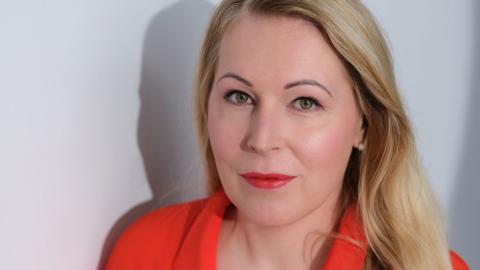 Irene looks straight into the camera wearing a bright red shirt.