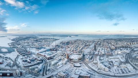 Snowy Tampere spreads out. In the middle is the Nokia Arena and the criss-crossing roads, with lakes and blue skies in the background.
