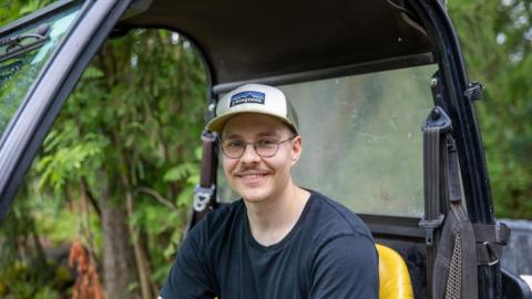 The person is sitting in a work vehicle and resting one hand on the steering wheel.