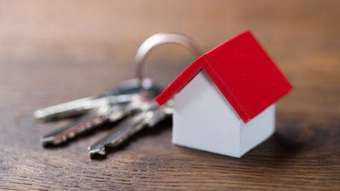 Avainnippu pöydällä ja avainperäksi on liitetty pieni punakattoinen valkoseinäinen mökki.