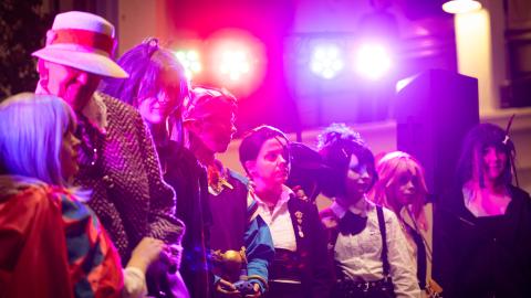 Lavalla värivalojen loisteessa cosplay asuihin pukeutuneita ihmisiä rivissä muotinäytöksessä..