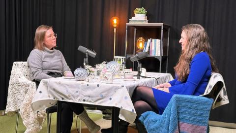 Aino-Maija Vaskelainen ja Anna-Kaisa Ikonen istuvat vastakkain pöydän äärellä podcast-studiossa. 