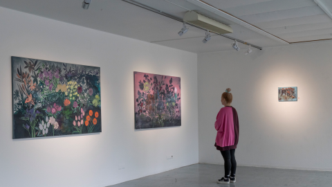 Henkilö katsoo värikkäitä ja suuria kukkatauluja taidegalleriassa.