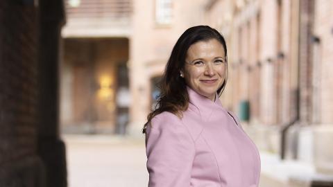Maria Nikkilä smiles at the camera, wearing a light pink wool coat. 