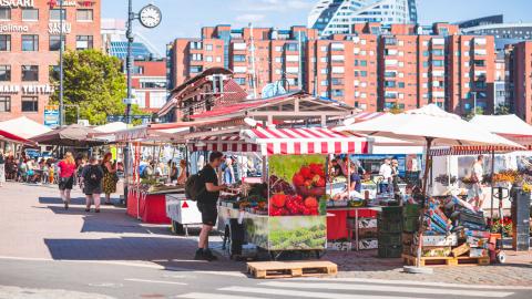 Colorful market stalls at sunny Laukontori, with brick-clad apartment buildings visible in the background.
