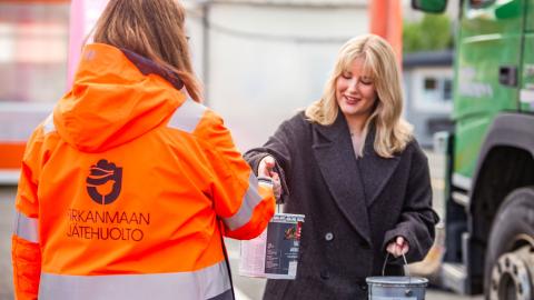 Jätehuollon työntekijä ottaa vastaa maalipurkkijätteet tuojalta.