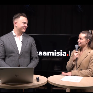 Mies kannettavan tietokoneen kanssa ja nainen mikrofoni kädessä juttelevat.